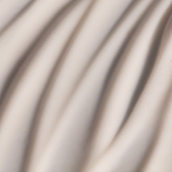 Creamy, pale surface with subtle wavy folds beside Odacité Retinol Therapy Hand Cream with PHA + Peptides tube.