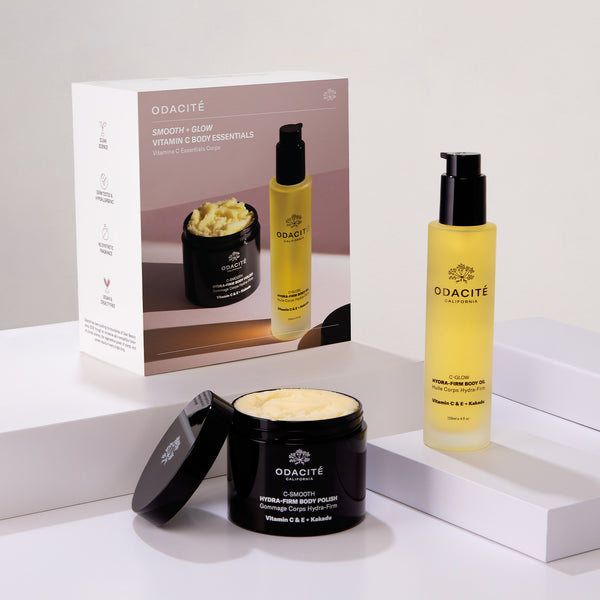 Odacité Smooth & Glow Vitamin C Body Essentials set with body polish, body oil, and box arranged on white block displays.