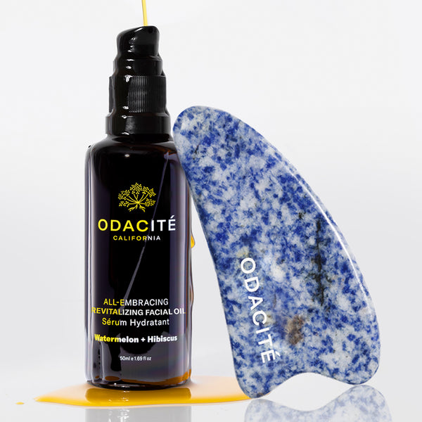 Odacite Gua Sha Facial Massage Set with a facial oil bottle beside a blue and white Gua Sha tool; oil drips onto the surface.