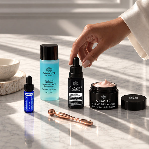 Hand reaching for Odacité Fall Reset Box and rose gold face roller on a light-colored countertop.