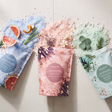 Three pouches of Odacite Relax & Recenter Bath Set arranged with crystals, grapefruit slices, lavender sprigs, and eucalyptus leaves.