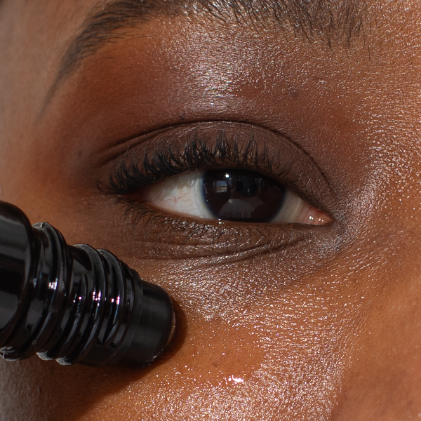 Hand applying Odacité Day & Night Eye Care Duo roller under eyes, focusing on dark circles; close-up view of application.