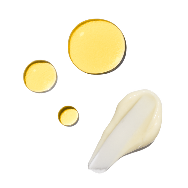 Three golden droplets of oil cleanser from the Sensitive Skin Double Cleansing Set next to a smear of creamy white rejuvenating cleanser.