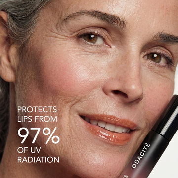 Woman smiling and holding Odacité SPF 40 Nourishing Lip Serum in a small tube, label visible.