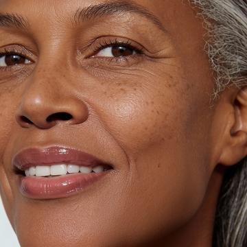 Smiling older woman holding Odacité SPF 40 Nourishing Lip Serum in sleek tube, natural skin and visible confidence.