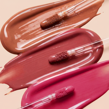 Odacité SPF 40 Nourishing Lip Serum applicators on brown, mauve, and pink gloss swatches, lined up diagonally on a light background.