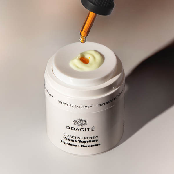 A dropper dispenses serum onto Odacité Structural Reset Duo: Supreme Cream & Bu+L, both in clear jars on a white surface.