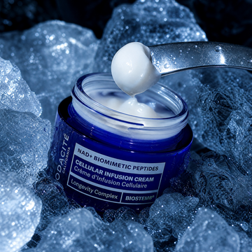 A blue cosmetic jar labeled BIOSTEM Cellular Infusion Cream sits in ice, with a metal spoon lifting a dollop of white cream above the open container.