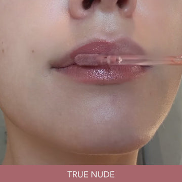 Close-up video of lips being coated with the Odacité SPF 40 Nourishing Lip Serum in True Nude, a soft rose-brown shade with a glossy, nourishing finish. The applicator wand glides the serum across closed and parted lips. Text overlay reads: TRUE NUDE.