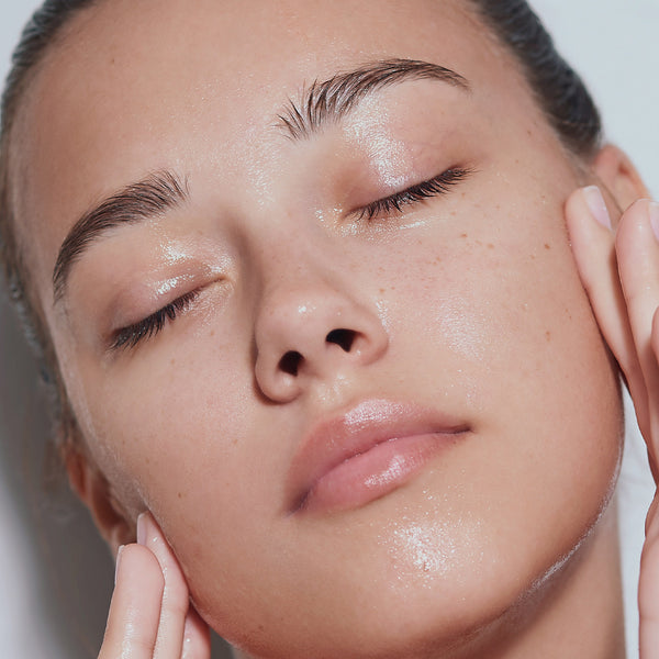 Person with radiant skin touching their face, next to Odacité Sensitive Skin Double Cleansing Set bottles.