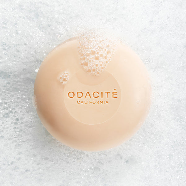 Odacite 552M Argan + Coconut Soap Free Shampoo Bar with bubbles sits on thick white foam and suds.