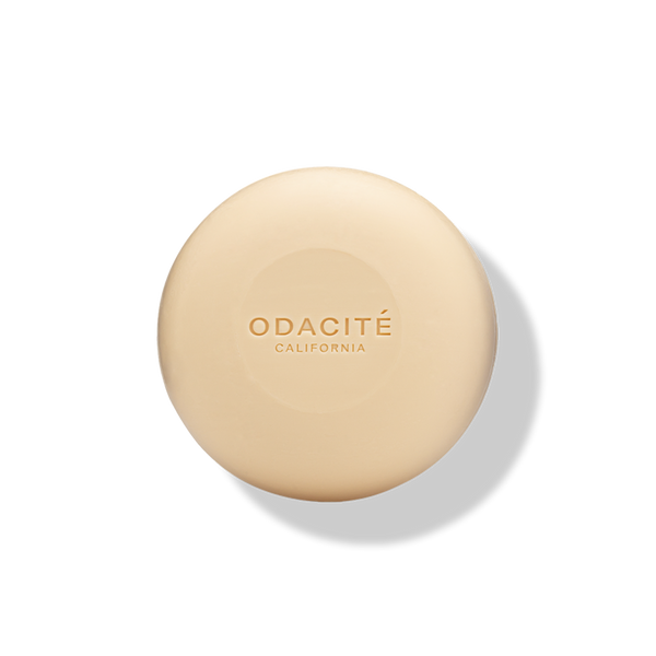 Round, beige ODACITÉ 552M Argan + Coconut Soap Free Shampoo Bar on a white background with a soft shadow.