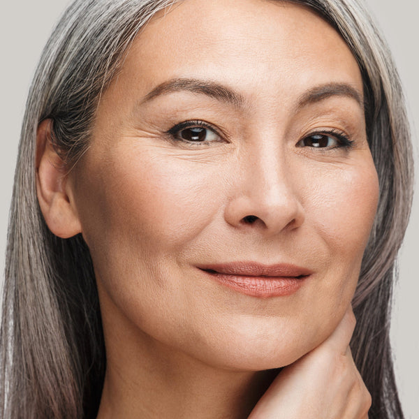 Woman with long gray hair and clear skin applies Odacite Ageless Skin + Eye Contour Duo to her face.