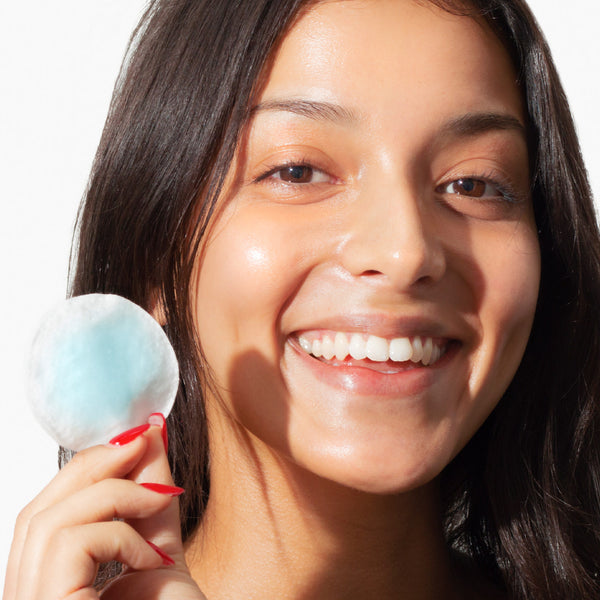 Woman holding Odacité Mature Skin Double Cleansing Set cleanser and cotton pad near her cheek, white background.