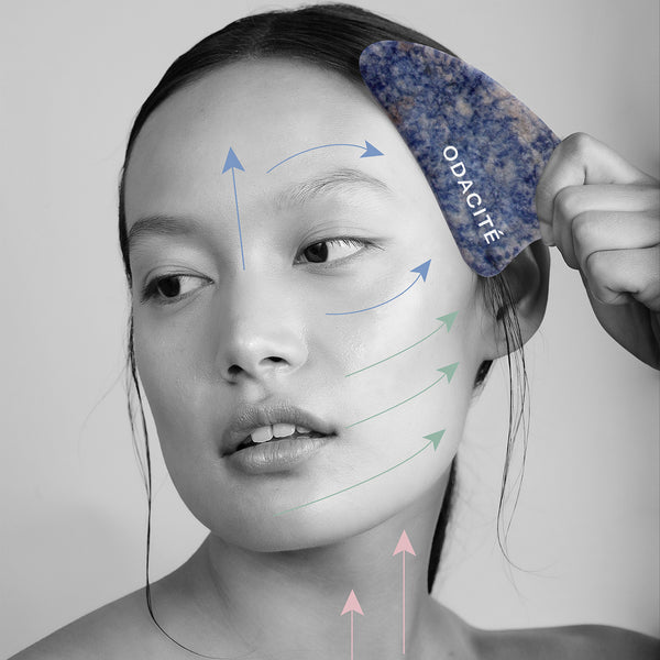 Woman massages cheek and neck with Odacite Crystal Contour Blue Sodalite Gua Sha, arrows show direction of use.