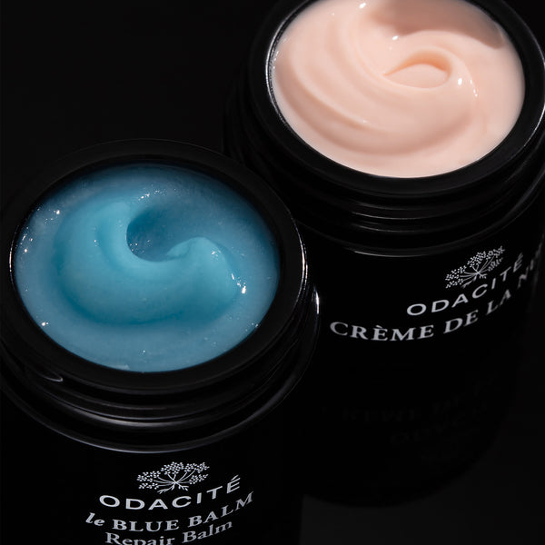 Odacité Deep Moisture Duo with open containers: blue repair balm and peach Vitamin C crème on a black background.