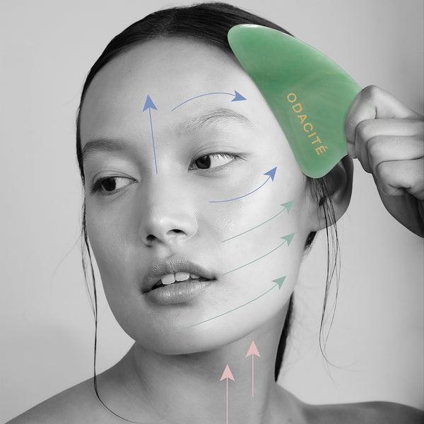 Woman using Odacite Crystal Contour Green Aventurine Gua Sha on her face, with colored arrows showing massage directions.