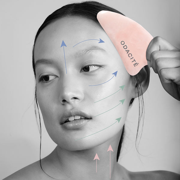 A woman massages her face with the Odacite Crystal Contour • Rose Quartz • Gua Sha. Colored arrows indicate upward strokes.