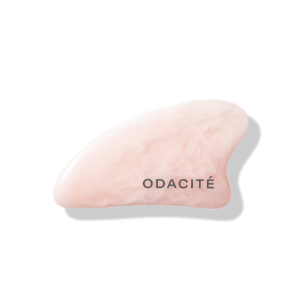 Odacite Crystal Contour Rose Quartz Gua Sha, pale pink stone with curved edges, rests on a light gray background.